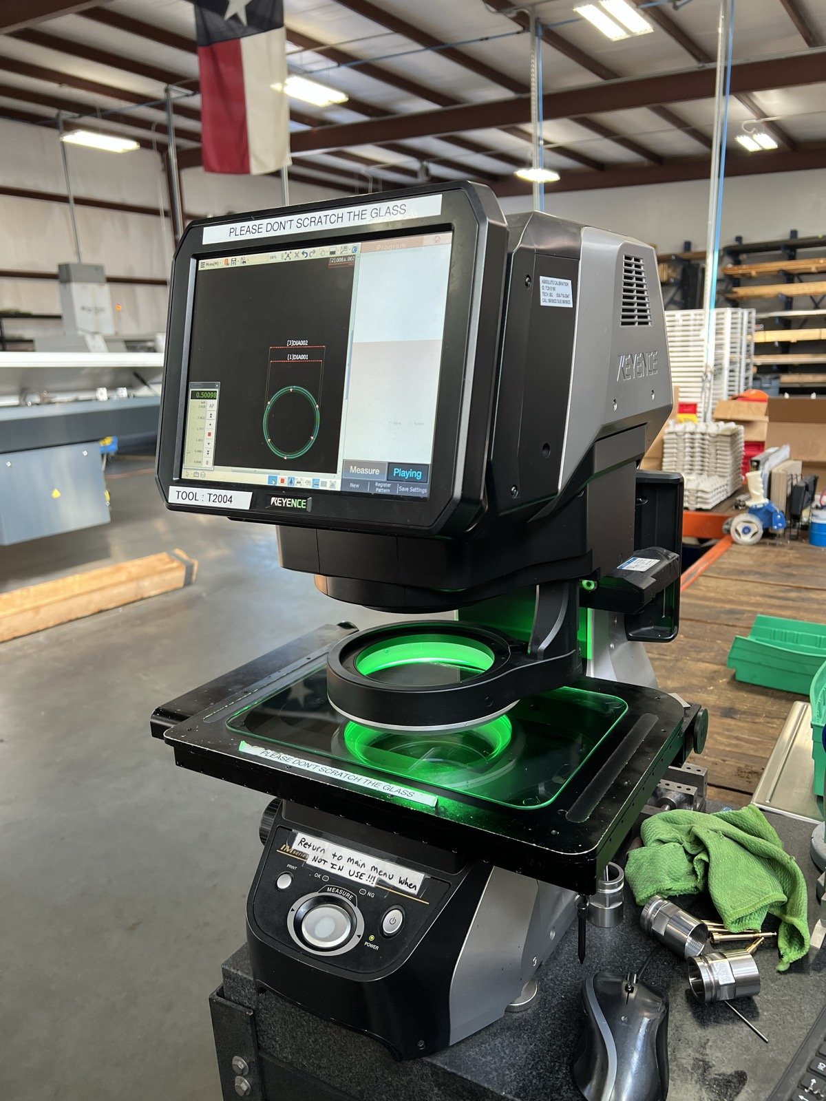 TXSwiss Keyence IM-Series optical comparator measuring a precision-machined ring under green LED transmitted light, dimensional inspection at the Conroe, Texas quality control lab